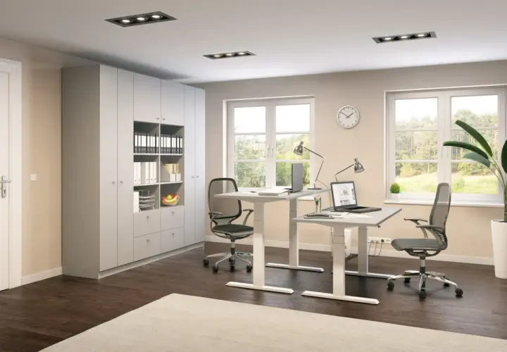 Modernes Arbeitszimmer einrichten: Zwei höhenverstellbare Schreibtische mit Laptops, Bürostühle, ein großer Schrank und Fenster mit Blick ins Grüne.