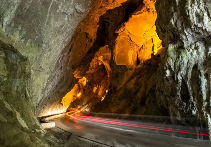 La cuevona, un túnel natural iluminado con luces cálidas, por donde pasan estelas rojas de vehículos.