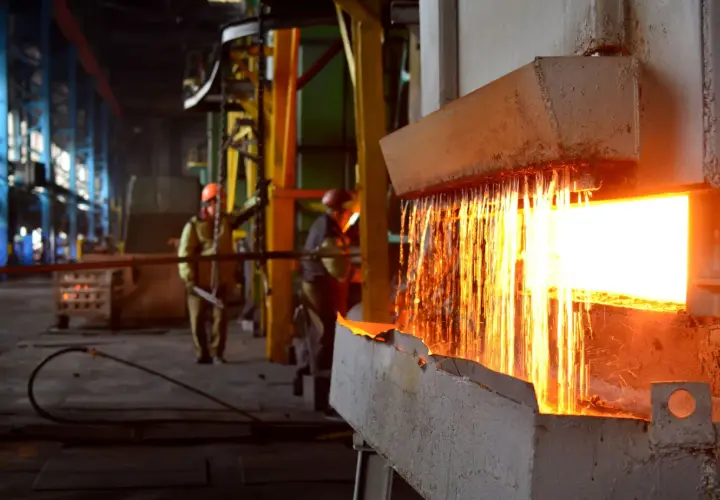 Gorący metal spływa podczas wyżarzania stali. Pracownicy w hełmach nadzorują proces w hucie.