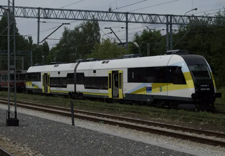 Nowy pociąg SA133-008, typu Pesa Elf, z charakterystycznym malowaniem w barwach żółto-biało-niebieskich, stoi na torach. Obok widoczny starszy wagon.
