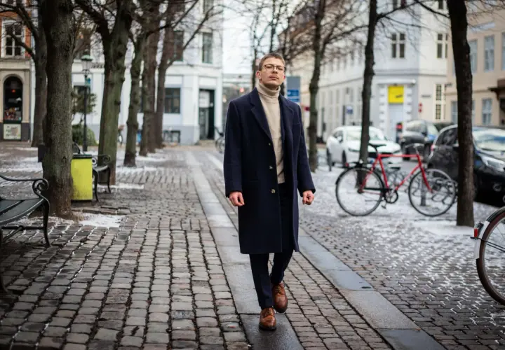 Elegancki mężczyzna w granatowym płaszczu i golfie spaceruje po zimowej ulicy. Stylowe granatowy płaszcz stylizacje na chłodne dni.