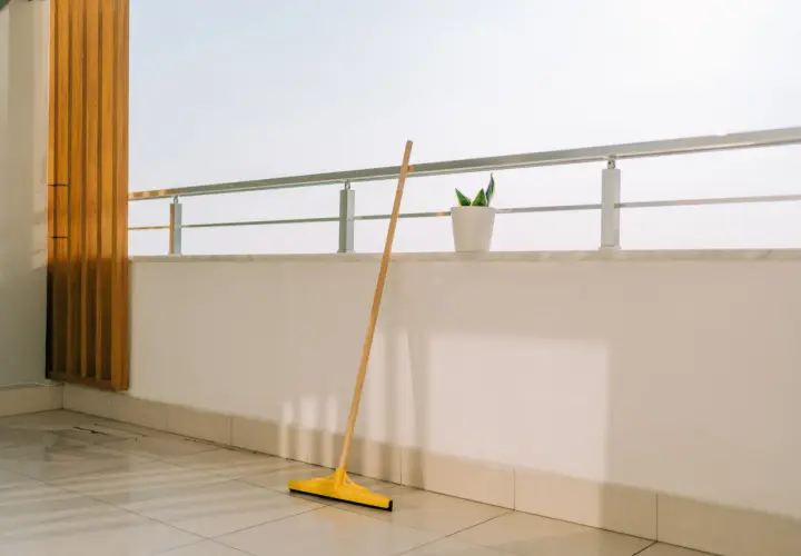 Scopa gialla appoggiata sul pavimento piastrellato, pronta per pulire la veranda del balcone.