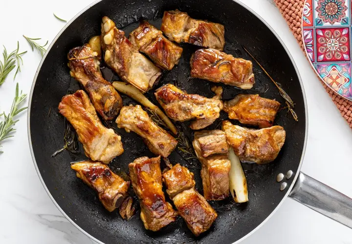 Costine di maiale in padella, dorate e succulente, con rosmarino e aglio. Un piatto invitante pronto per essere gustato.
