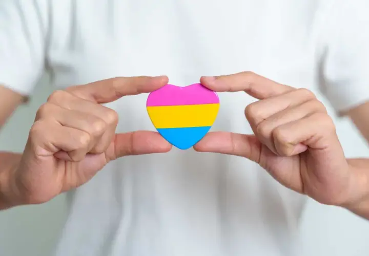 Dłonie trzymają serce w kolorach pan orientacji: różowym, żółtym i niebieskim.