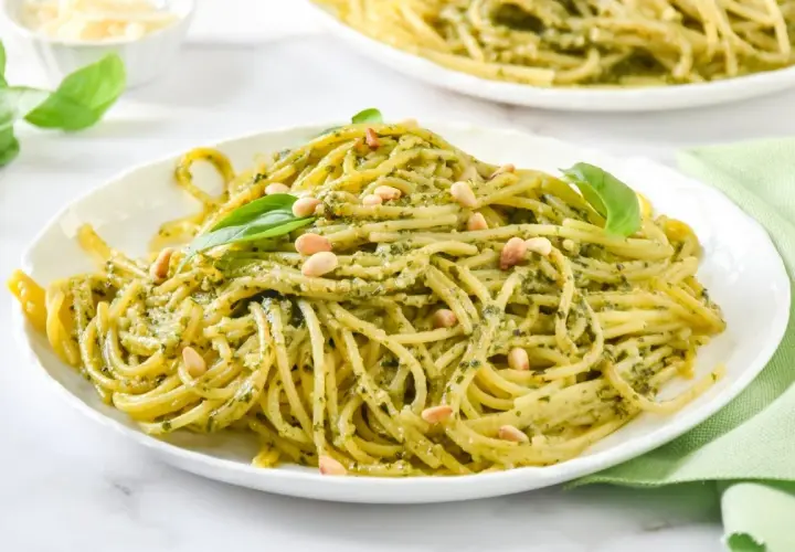 Un plato de espaguetis al pesto, cubierto con piñones y hojas de albahaca fresca.