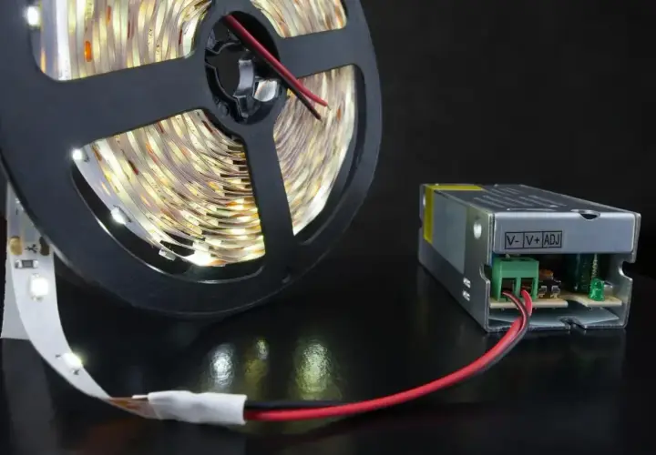 Zasilacz do taśmy LED 12V GU10 i zwinięta taśma LED na czarnym tle.