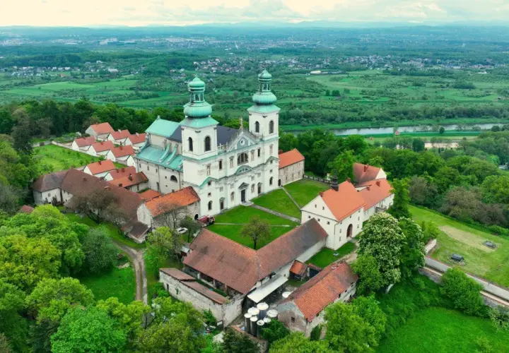 Malowniczy klasztor kamedułów Kraków na wzgórzu, otoczony zielenią, z widokiem na dolinę Wisły i miasto w oddali.