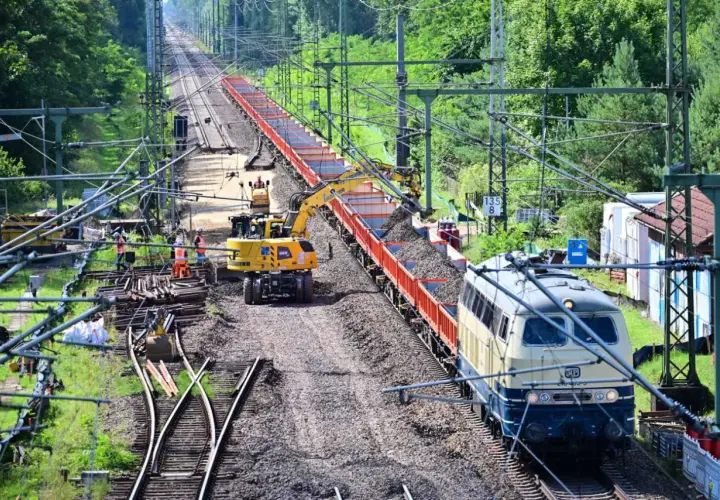 Gleisbauarbeiten: Bagger beladen einen Güterzug mit Schotter.