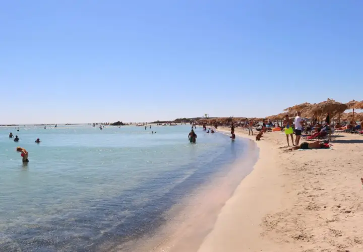 Słoneczna plaża Elafonisi z turkusową wodą, piaskiem i ludźmi odpoczywającymi pod parasolami.