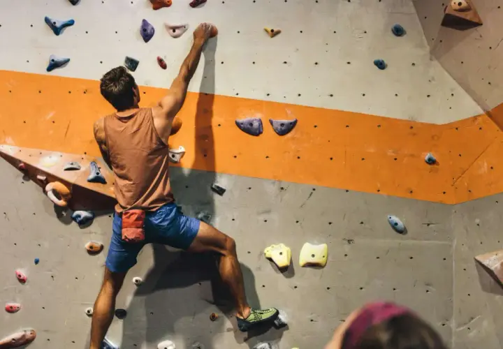 Mężczyzna wspina się po ścianie w hali do boulderingu. To świetny sposób na aktywność fizyczną i rozwijanie siły.