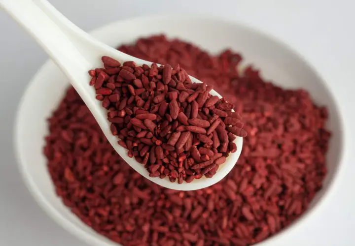 Un cucchiaio bianco pieno di riso rosso fermentato, un alimento noto per i suoi benefici. Per quanto tempo assumerlo? Chiedi al tuo medico.
