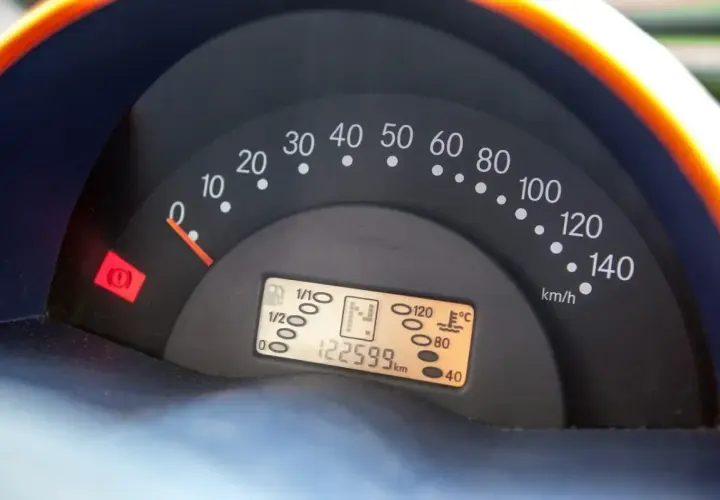 Cruscotto auto con tachimetro, indicatore carburante e spia freno a mano accesa. Chilometraggio 122599 km.
