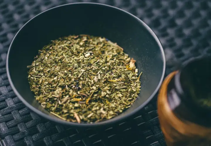 Suszone liście i gałązki, z których jest yerba mate, w czarnej miseczce obok tykwy.