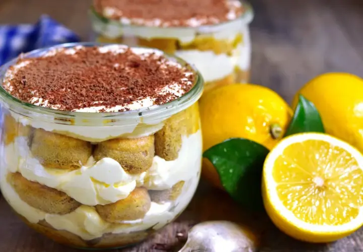 Pyszne tiramisu cytrynowe w słoiczku, przełożone biszkoptami i kremem, posypane czekoladą. Obok świeże cytryny.