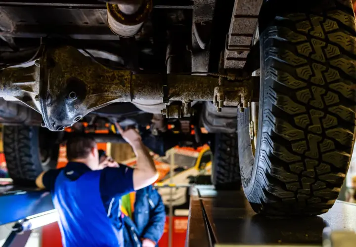 Mechanik sprawdza podwozie terenowego auta z napędem **awd**. Widoczna jest piasta, opona i elementy zawieszenia.
