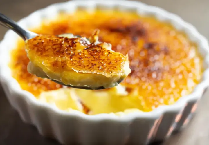 Une cuillère soulève une bouchée de crème brûlée clementine, révélant sa croûte caramélisée craquante et sa crème onctueuse.