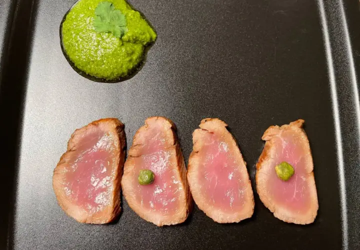 Cuatro lonchas de tataki de salmón con un toque de salsa verde y alcaparras, servidas en plato negro.