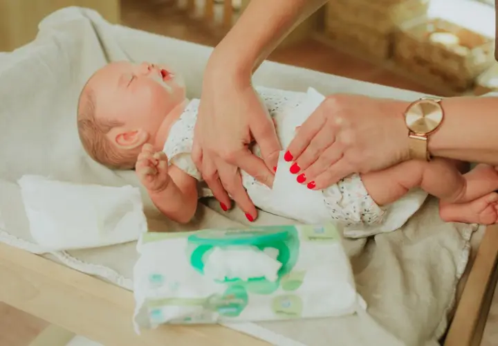 Delikatne dłonie z czerwonymi paznokciami pokazują, jak przewijać noworodka, używając chusteczek nawilżanych.