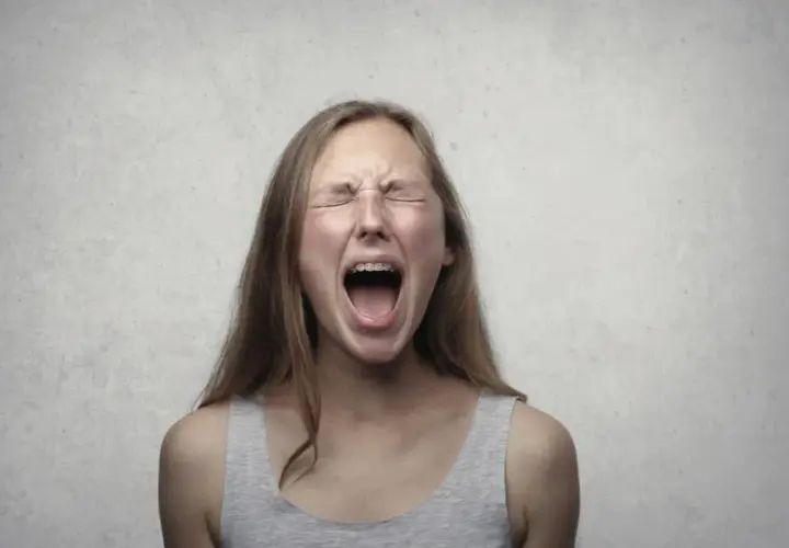 Ragazza con apparecchio dentale urla, occhi chiusi e fronte corrugata, un'espressione di pura paura di perdere il controllo.