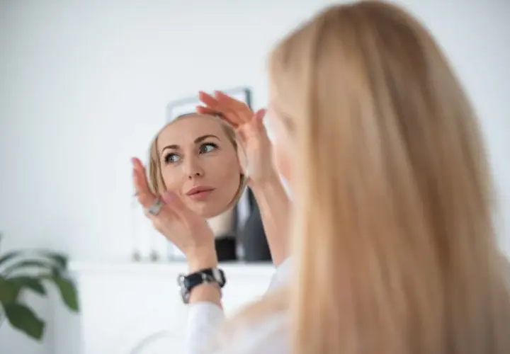 Kobieta z blond włosami ogląda swoją twarz w lusterku.
