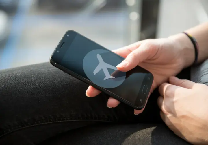 Dłoń trzyma smartfon z ikoną samolotu. Zastanawiasz się, czy w trybie samolotowym działa budzik?