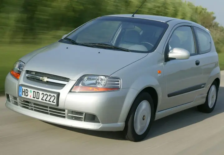 Srebrny Chevrolet Kalos w wersji 3-drzwiowej jedzie po drodze, rozmyte tło sugeruje ruch.