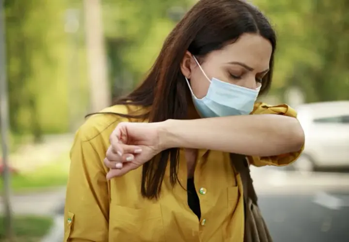 Mujer con mascarilla quirúrgica para que sirve, tose en el codo para evitar contagios.