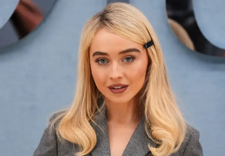 Mujer rubia con raya del pelo lateral, ojos azules y un clip negro en el cabello.