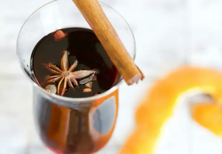 Un verre de vin chaud aux épices, parfait pour un marché de Noël. Une étoile de badiane et un bâton de cannelle flottent dans le liquide sombre.
