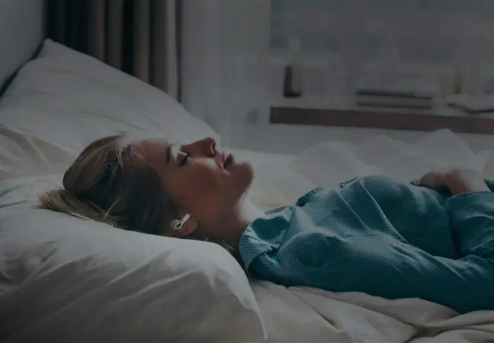 Kvinna med hörlurar i sängen, lyssnar på guidad meditation för avkoppling.