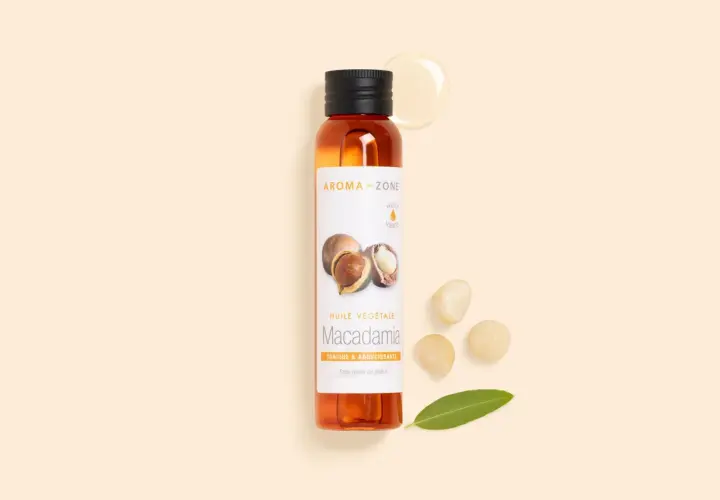 Flacon d'huile de macadamia, ses bienfaits pour la peau sont nombreux. Noix et feuille à proximité.