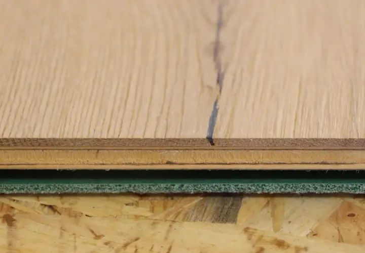 Detailaufnahme von Holzschichten und grüner Trittschalldämmung, bereit für das Parkett verlegen.