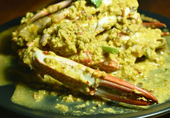 Krab w żółtym sosie curry na czarnym talerzu.