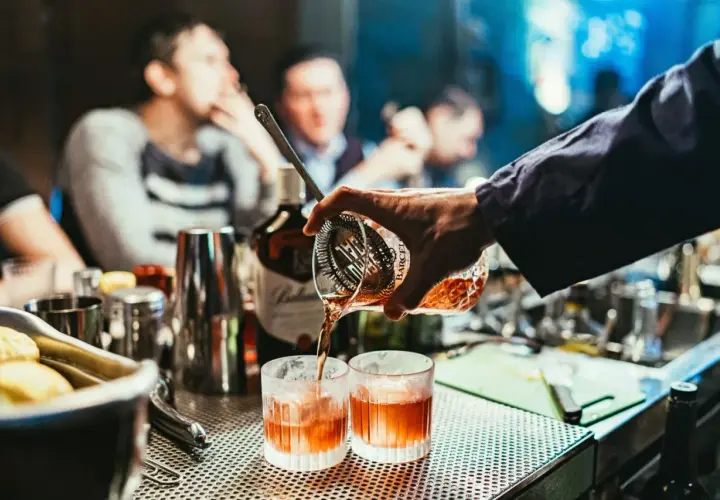 Un barman prépare un cocktail de base, versant un liquide ambré dans deux verres.