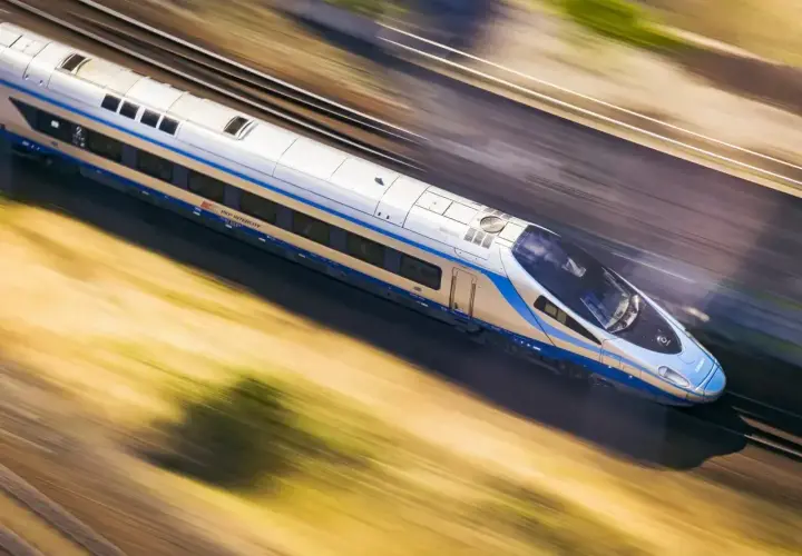 Srebrno-niebieski pociąg PKP Intercity mknie po torach, ukazując imponującą prędkość pociągu.