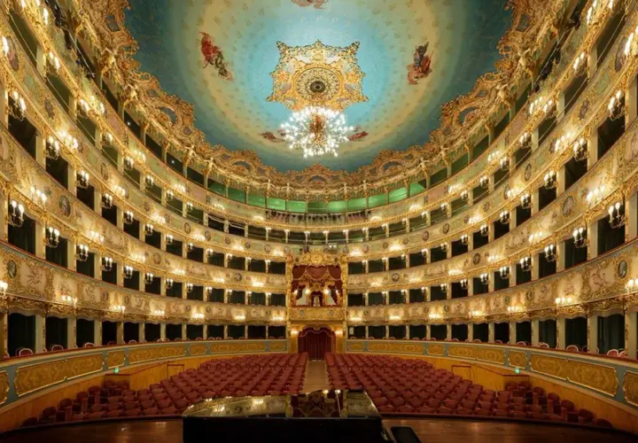 L'intérieur doré et orné du théâtre La Fenice, avec ses loges superposées, ses lustres étincelants et son plafond peint, prêt à accueillir un concert.