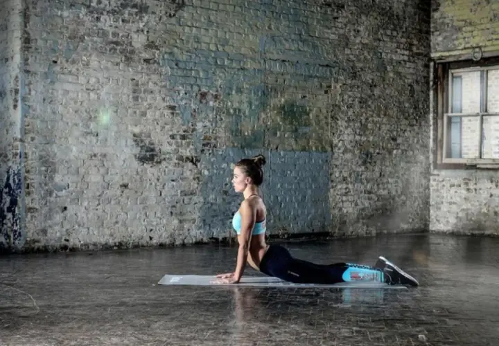 Kobieta ćwicząca pilates w pozycji kobry na macie w industrialnym wnętrzu.