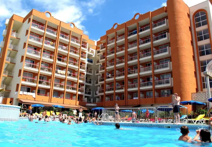 Gente disfrutando en la piscina del hotel Belvedere Salou, con edificios naranjas y blancos de fondo.