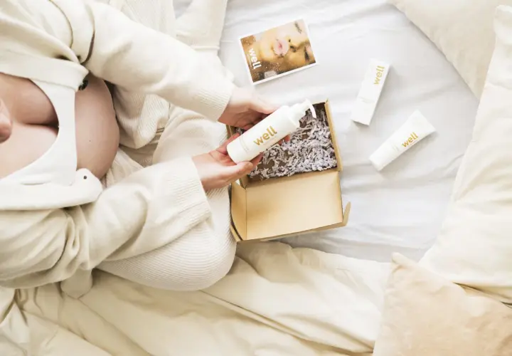 Gravid kvinna öppnar ett paket med hudvårdsprodukter. En flaska med hyaluronsyra och en kräm för bristningar är synliga.