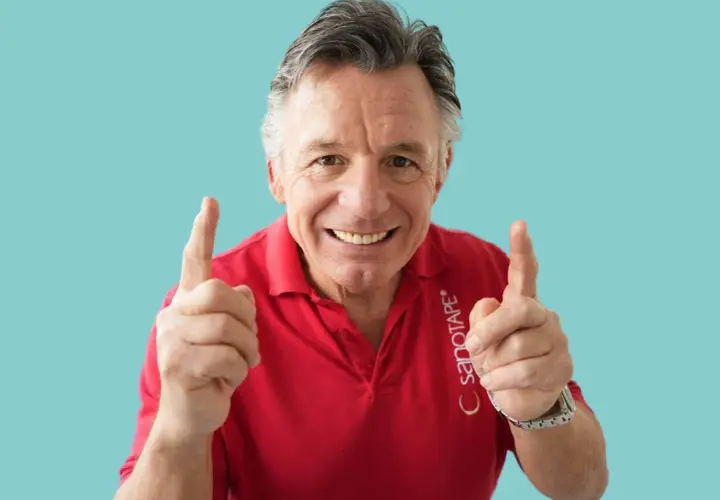 Steffen Barth zeigt mit beiden Zeigefingern nach oben und lächelt. Er trägt ein rotes Poloshirt mit dem Aufdruck "SANOTAPE".