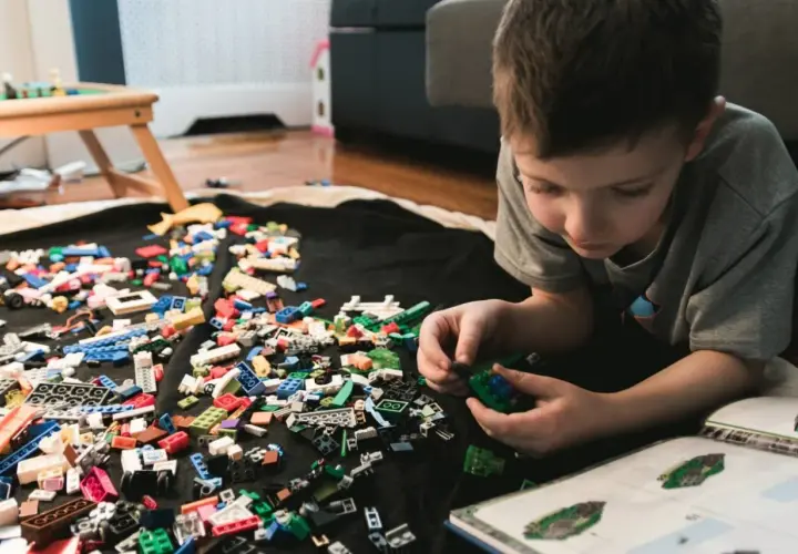 Chłopiec buduje z klocków LEGO, a obok leży instrukcja. Jak umyć klocki LEGO? Wystarczy je zebrać i umyć.