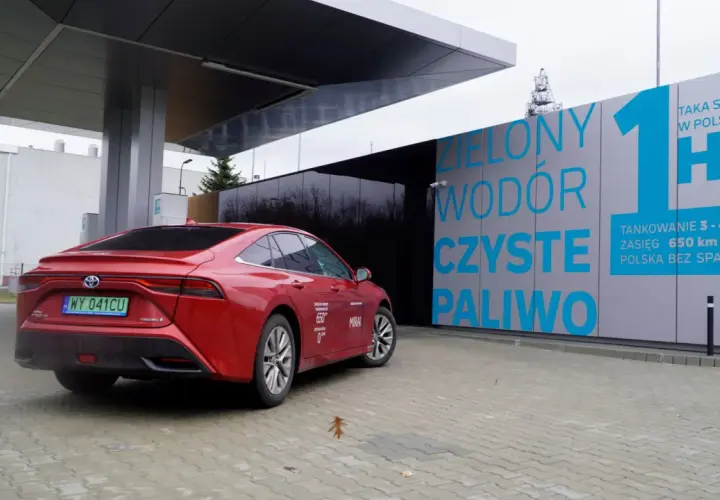 Czerwona Toyota Mirai na stacji tankowania wodoru. "Zielony wodór, czyste paliwo" - hasła na budynku stacji.