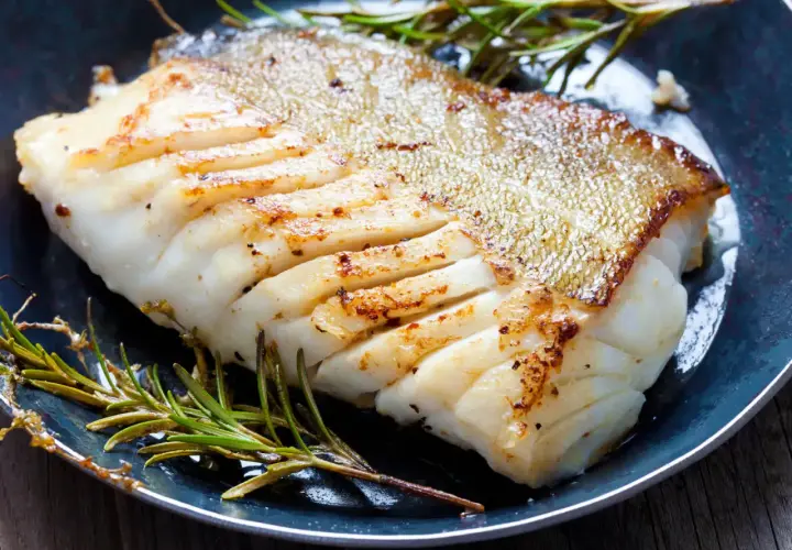 Un filet de poisson blanc parfaitement cuit, peau dorée et chair nacrée, servi avec du romarin frais. Une belle illustration de comment cuire du poisson blanc.