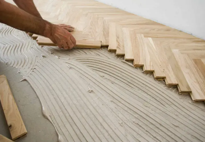Pose de parquet en chevrons. Des lames de bois clair sont posées sur un lit de colle ondulée.