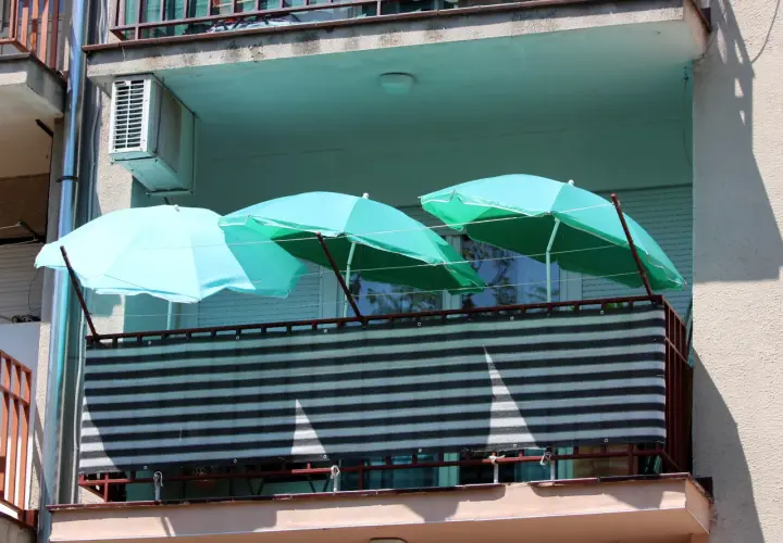 Trzy turkusowe parasole nad zasłoniętą balustradą na balkonie. Pomysł, jak zasłonić balustradę na balkonie, wykorzystując parasole.