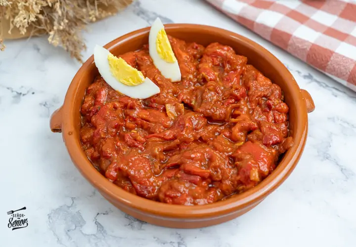 Un plato de asadillo manchego, con pimientos rojos guisados y adornado con gajos de huevo cocido.