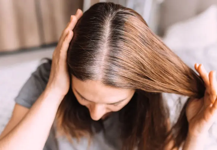 Una mujer se toca el cabello, mostrando mechones grises que explican porque salen canas.