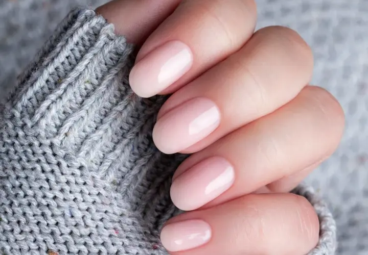 Dłoń z delikatnym, różowym manicure. Czy baza kauczukowa niszczy paznokcie? Zdjęcie sugeruje, że nie, jeśli jest stosowana prawidłowo.