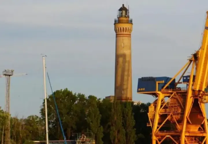 Najwyższa latarnia morska w Polsce, strzegąca portu, góruje nad żółtymi dźwigami i zielenią.