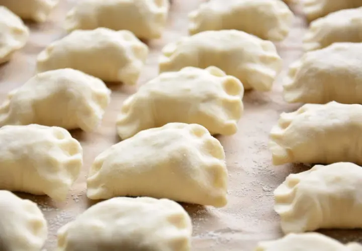 Gotowe do gotowania pierogi ruskie, przygotowane według tradycyjnego przepisu. Widać je ułożone rzędami na blacie.